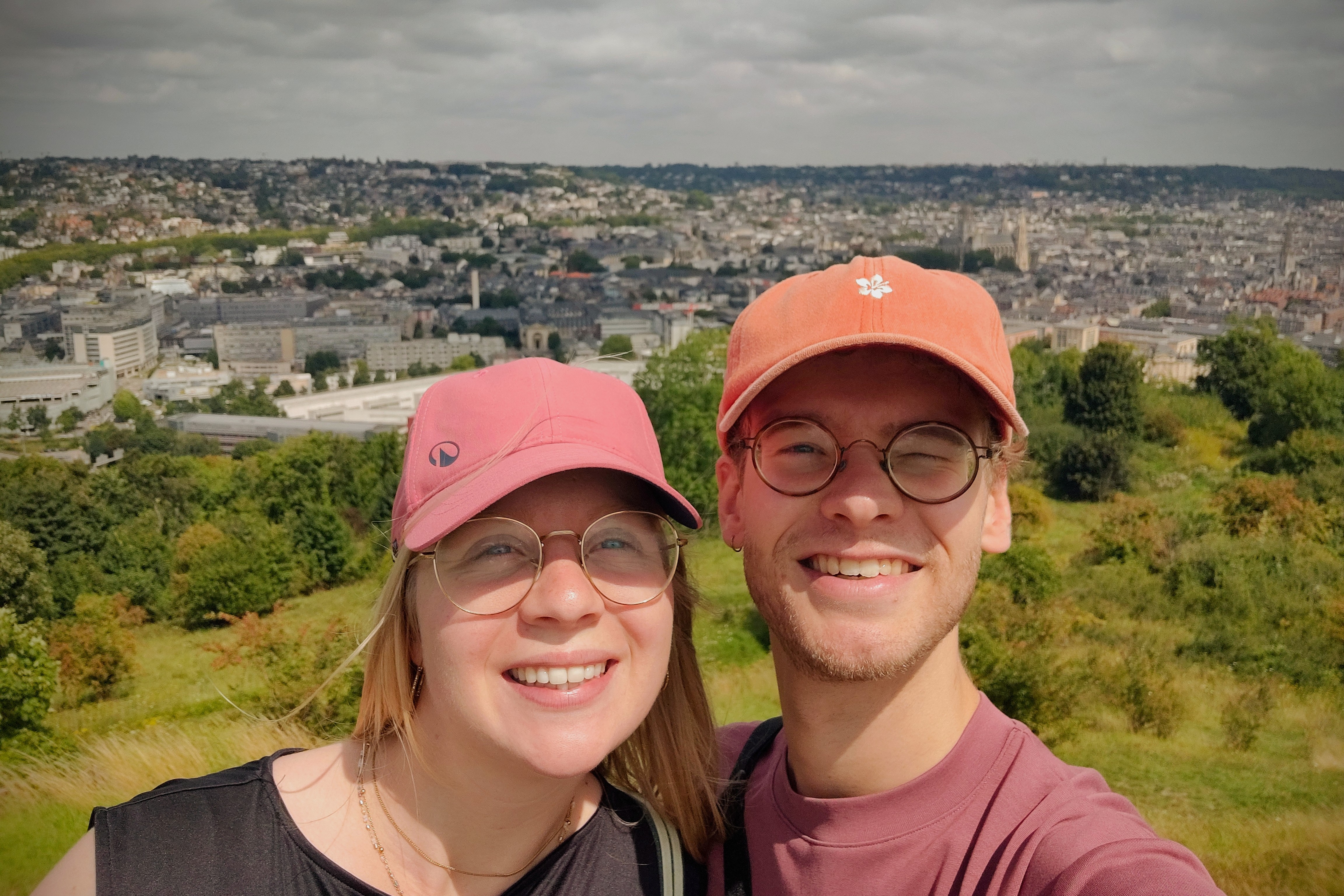 Two people smiling at a scenic viewpoint overlooking a city